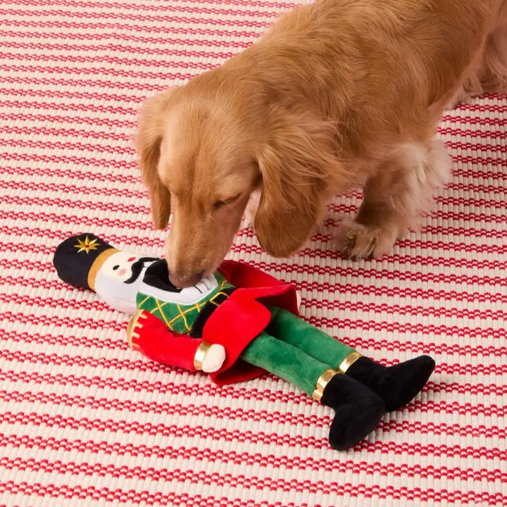Dog playing with a Christmas-themed toy on a red and white striped blanket