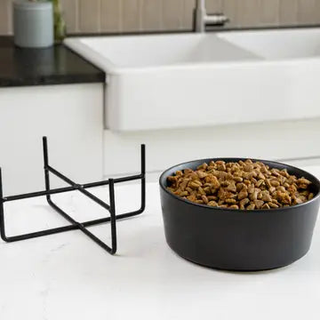 Black elevated pet feeder and bowl with pet food on a kitchen counter.